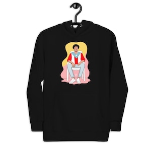 Puede incluir: Sudadera con capucha negra con un gráfico de una persona sentada en una silla. La persona lleva una camisa roja, blanca y azul con una estrella. El fondo es amarillo y rosa.