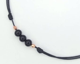 May include: A black cord necklace with three black beads and gold accents.