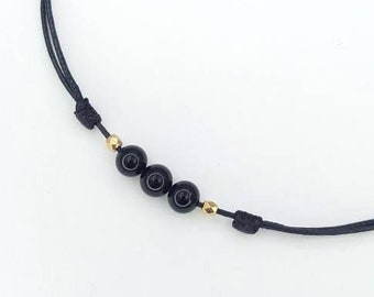 May include: A simple black cord necklace with three black beads and gold accents.