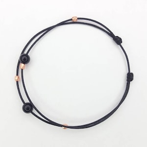 May include: A black cord bracelet with black beads and rose gold accents.