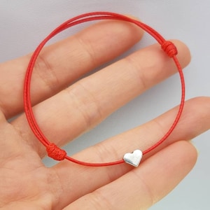 May include: Red string bracelet with a silver heart charm.