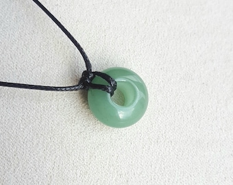 May include: A green stone pendant with a hole in the center, hanging from a black cord.