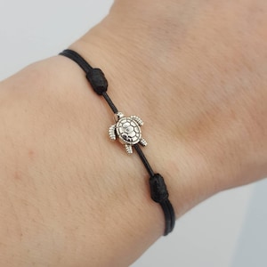 May include: A black string bracelet with a silver turtle charm. The bracelet is adjustable and has a simple design.