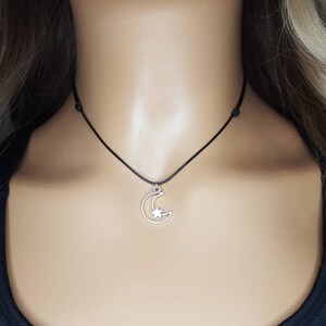 May include: A silver crescent moon charm with a star inside, hanging from a black cord necklace.