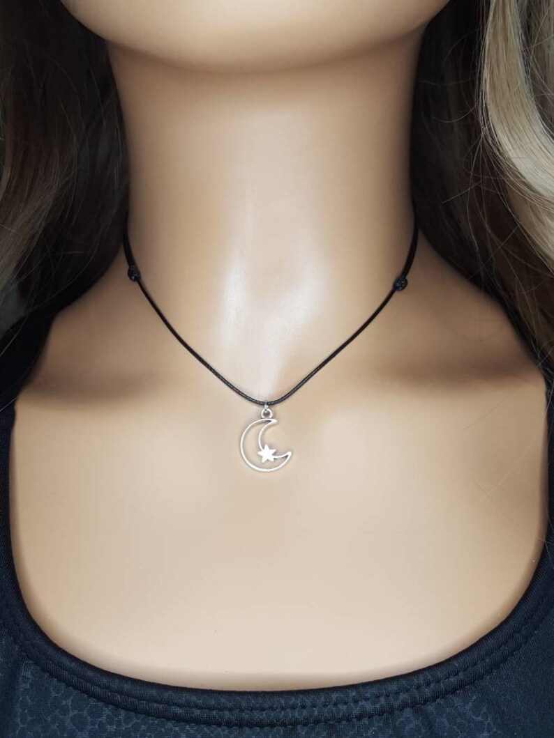 May include: A silver crescent moon charm with a star inside, hanging from a black cord necklace.