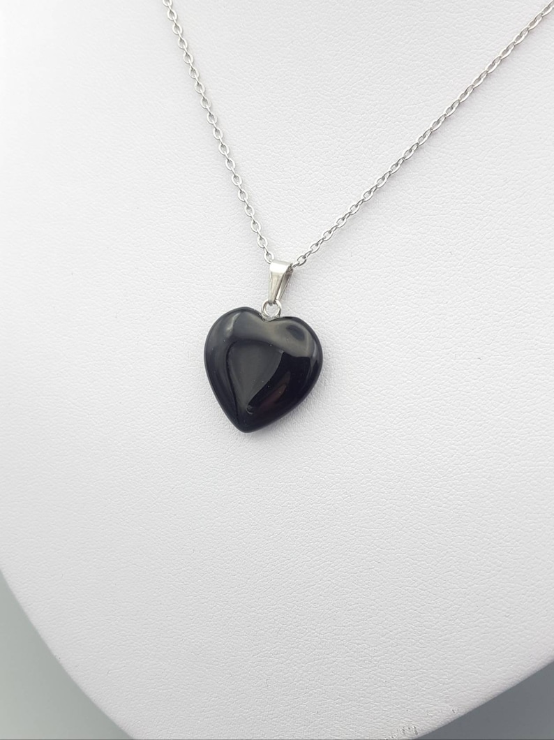 May include: A silver chain necklace with a black heart-shaped pendant.