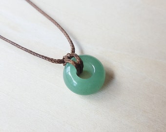 May include: A green jade stone pendant in the shape of a ring, hanging from a brown cord necklace.