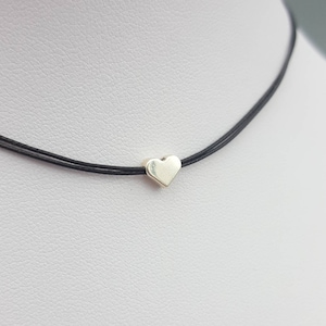 May include: A simple silver heart charm necklace on a black cord.