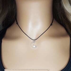 May include: A silver crescent moon charm with a star inside hangs from a black adjustable cord necklace. The necklace is adjustable from 13 to 25 inches.