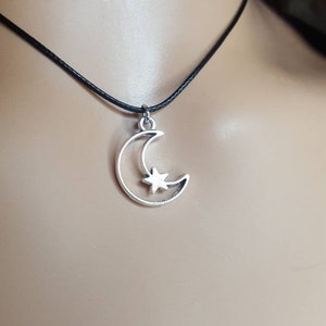 May include: A silver crescent moon charm with a star inside, hanging from a black cord necklace.