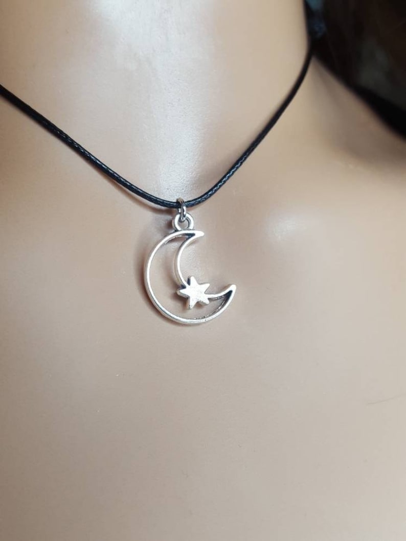 May include: A silver crescent moon charm with a star inside, hanging from a black cord necklace.