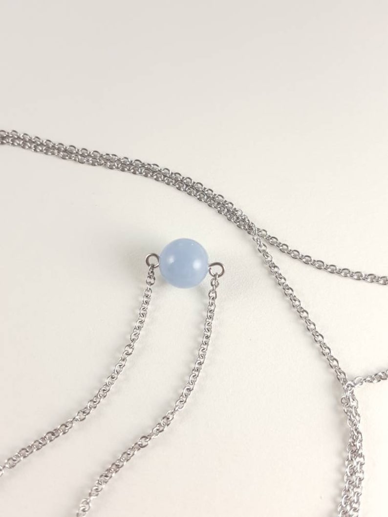 K&ouml;nnte beinhalten: Eine zarte Halskette mit einem hellblauen, kugelf&ouml;rmigen Perlenanh&auml;nger. Der Anh&auml;nger ist an einer feinen, silberfarbenen Kette befestigt. Die Halskette hat ein mehrschichtiges Design mit mehreren Kettengliedern.