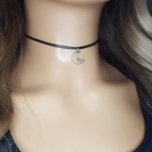 May include: A black choker necklace with a silver crescent moon charm with a small star inside.