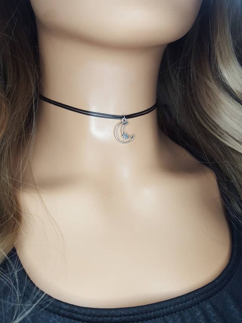 May include: A black choker necklace with a silver crescent moon charm with a small star inside.