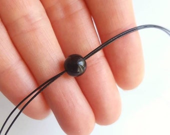 May include: A black cord necklace with a single black bead.