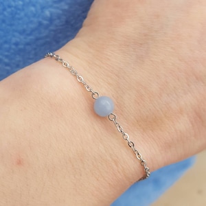 May include: A delicate silver chain bracelet with a single light blue gemstone bead.