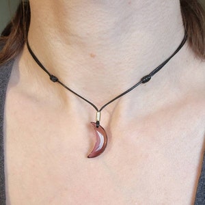 May include: A simple black cord necklace with a crescent moon pendant made of clear glass with a purple hue.