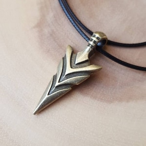 May include: A bronze arrowhead pendant necklace with a black leather cord. The arrowhead is detailed with a geometric pattern.