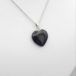May include: A silver chain necklace with a black heart-shaped pendant.