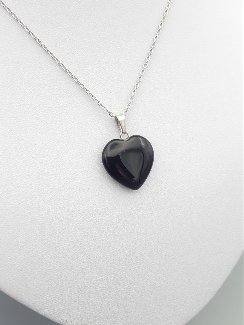 May include: A silver chain necklace with a black heart-shaped pendant.