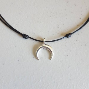 May include: A simple silver crescent moon pendant necklace on a black cord.