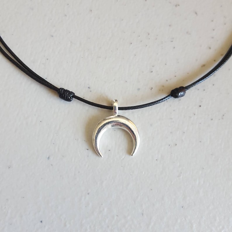 May include: A simple silver crescent moon pendant necklace on a black cord.