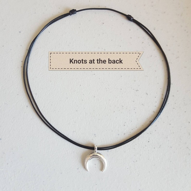 May include: A black cord necklace with a silver crescent moon pendant. The necklace has knots at the back.