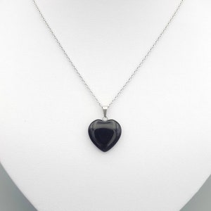 May include: A silver chain necklace with a black heart-shaped pendant.