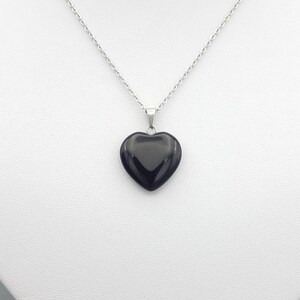 May include: A silver chain necklace with a black heart-shaped pendant.