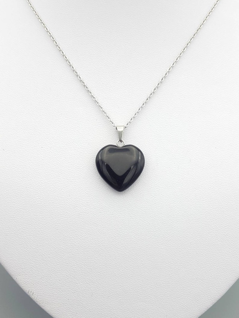 May include: A silver chain necklace with a black heart-shaped pendant.