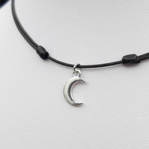 May include: A simple black cord necklace with a silver crescent moon pendant.