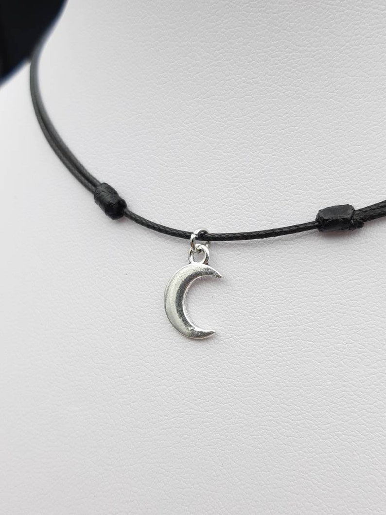 May include: A simple black cord necklace with a silver crescent moon pendant.