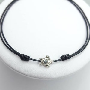 May include: A black string bracelet with a silver turtle charm.