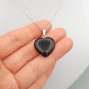 May include: A silver chain necklace with a black heart-shaped pendant.