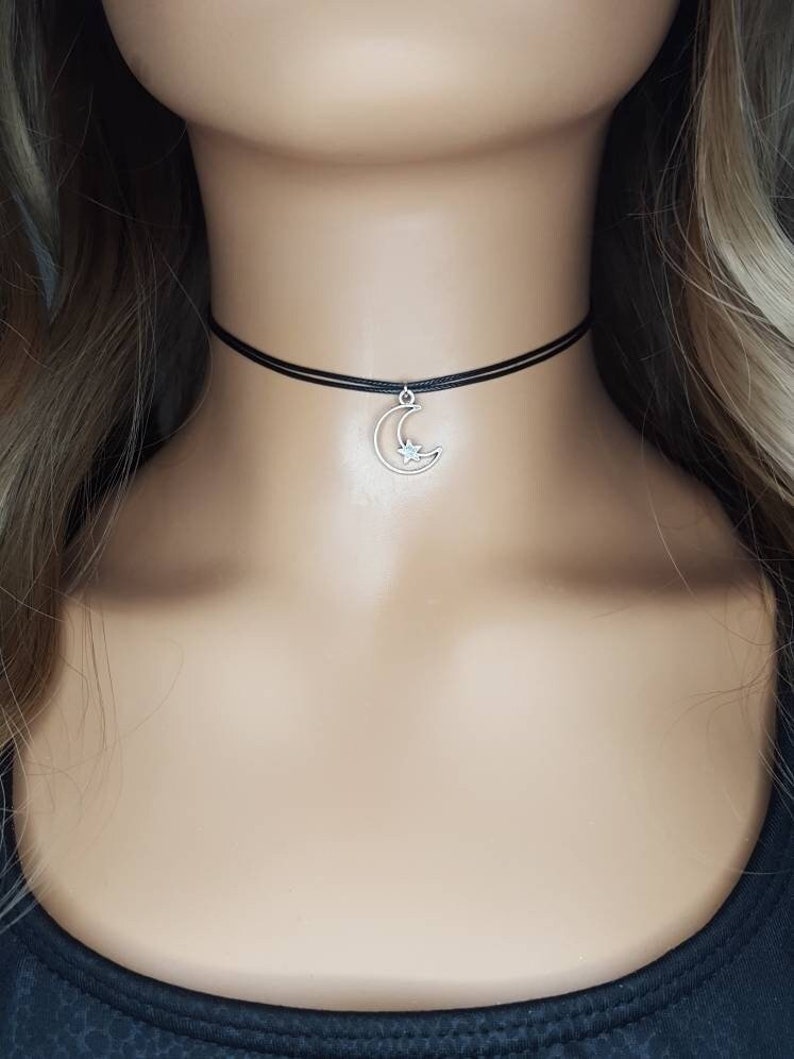 May include: A black choker necklace with a silver crescent moon charm with a small star in the center.