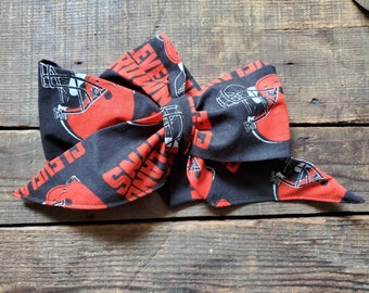 May include: A black and orange fabric bow with a repeated pattern of football helmets and the word "Browns".