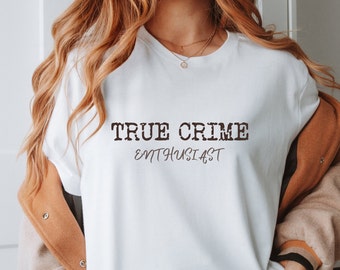Op de afbeelding: Wit T-shirt met de tekst "TRUE CRIME ENTHUSIAST" in bruin gedrukt op de voorkant.