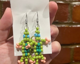 May include: A pair of green, blue and pink beaded earrings shaped like lizards. The earrings are hanging from silver hooks.