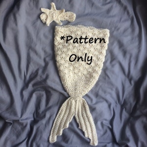 May include: A crocheted mermaid tail blanket in white with a matching starfish headpiece. The blanket is laid out on a gray fabric background. The text "*Pattern Only" is written on the blanket.