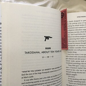 May include: A close-up of a book page with text about Star Wars: Last Shot. The text describes Han Solo's thoughts and feelings as he is on the planet Takodana. The page also features a small illustration of a blaster.