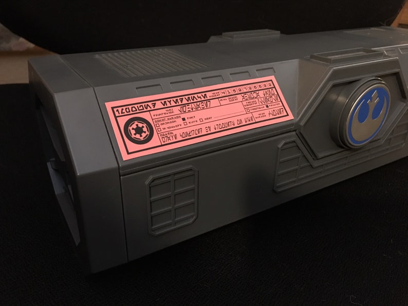 May include: A gray box with a pink label that says "1200000007 MYY7MI4M" and a Rebel Alliance symbol. The box also has a blue and silver Rebel Alliance symbol on the side.