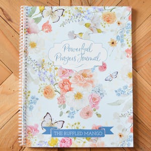 May include: A white journal with a floral design and the text "Powerful Prayers Journal" and "The Ruffled Mango" on the cover.