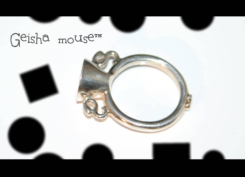 May include: A silver ring with a bell-shaped top and the text "Geisha mouse&trade;" on the side.