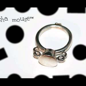 May include: A silver ring with a round, flat top and two small, curved details on either side. The ring is inscribed with the text "Geisha mouse&trade;".