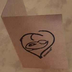 Peut inclure: Une carte rose avec un c&oelig;ur dessin&eacute; &agrave; la main en noir avec un visage &agrave; l'int&eacute;rieur. Le texte "REPHANICURE" est &eacute;crit sous le c&oelig;ur.