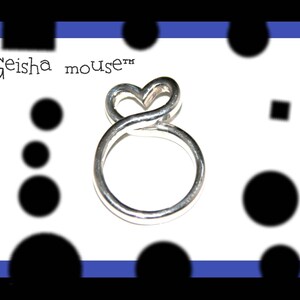May include: Silver ring with a heart-shaped design. The ring is made of twisted wire and has a smooth finish. The text "Geisha mouse&trade;" is visible in the background.