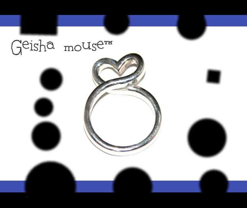 May include: Silver ring with a heart-shaped design. The ring is made of twisted wire and has a smooth finish. The text "Geisha mouse&trade;" is visible in the background.