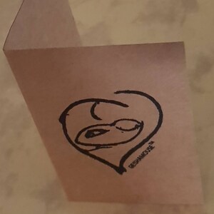 May include: A pink card with a black hand-drawn heart shape with a face inside. The text "REPHANICURE" is written below the heart.