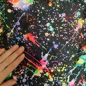 May include: Black fabric with a colorful paint splatter pattern. The fabric has a variety of colors including pink, blue, green, yellow, and orange.