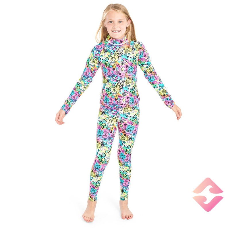 May include: A girl wearing a long-sleeved, colorful, patterned top and matching leggings. The pattern features peace signs, hearts, and other symbols.